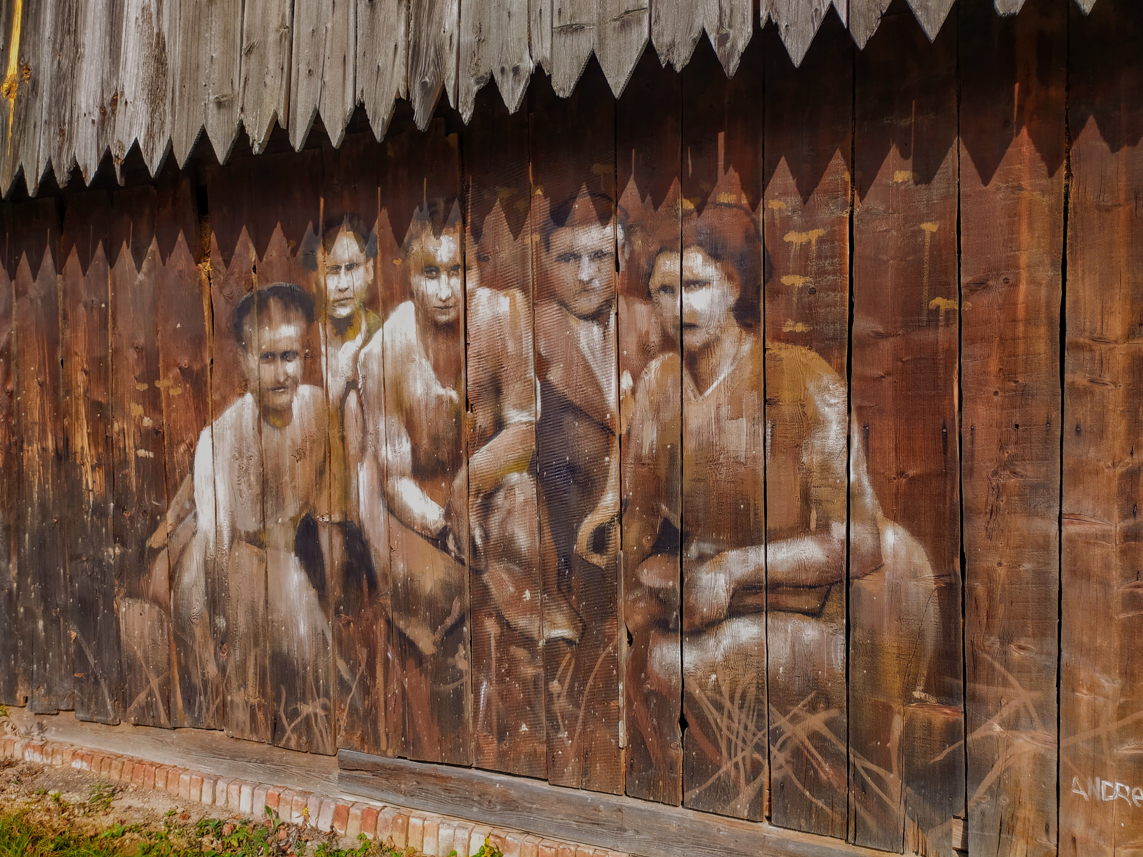 obraz malowany na deskach stodoły, przedstawiający odświętnie ubraną grupę pięciu osób, przykucnietych, pozujących do zdjęcia